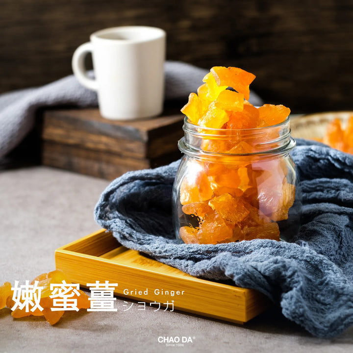 Jar of fried ginger on a wooden tray with a cup in the background