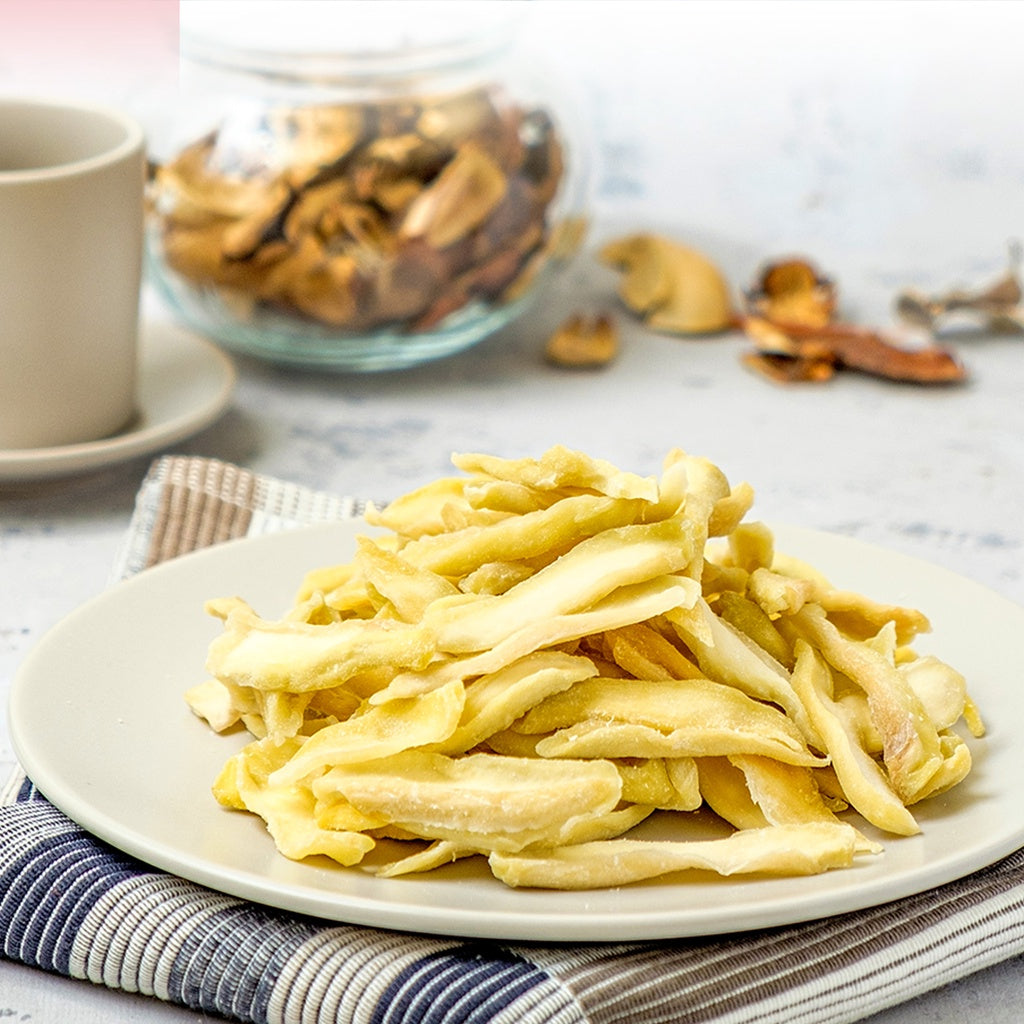 Dried green mango on a plate with a cup and jar in the background