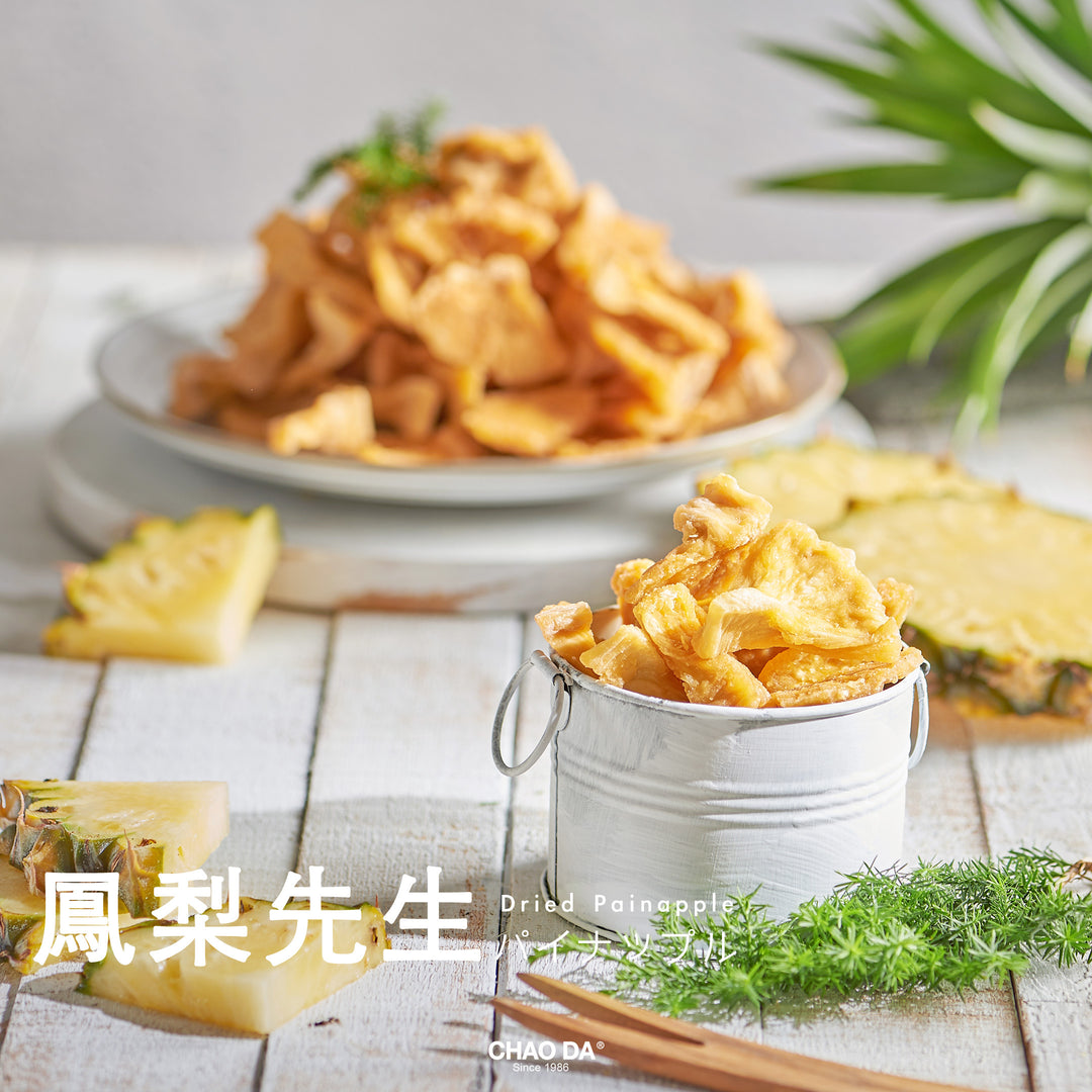 Dried pineapple slices in a small bucket with a plate of pineapple slices and a pineapple in the background on a wooden table.