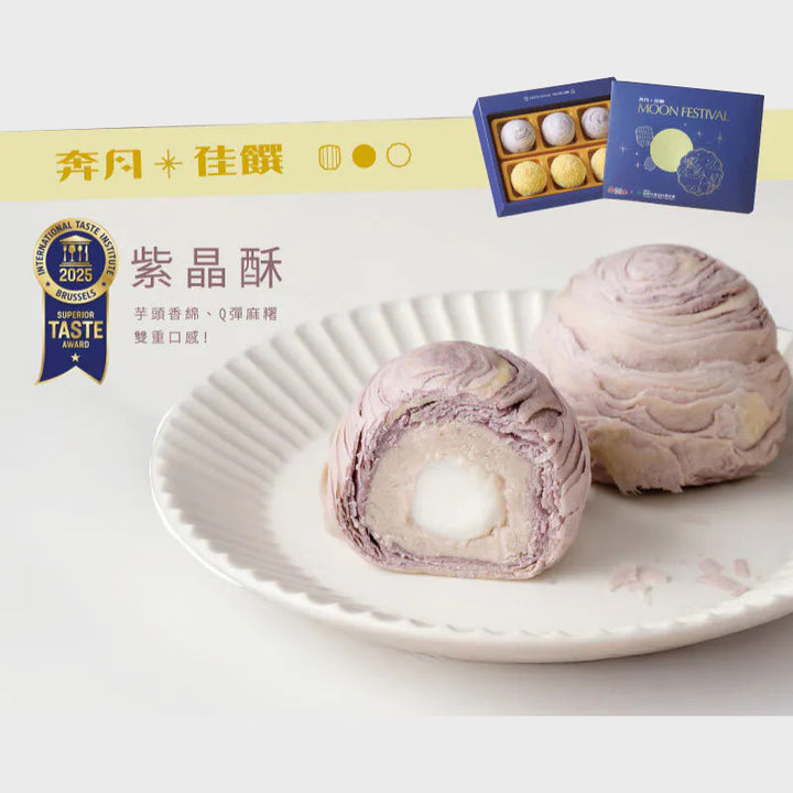 Two purple mooncakes on a white plate with a box of mooncakes in the background.