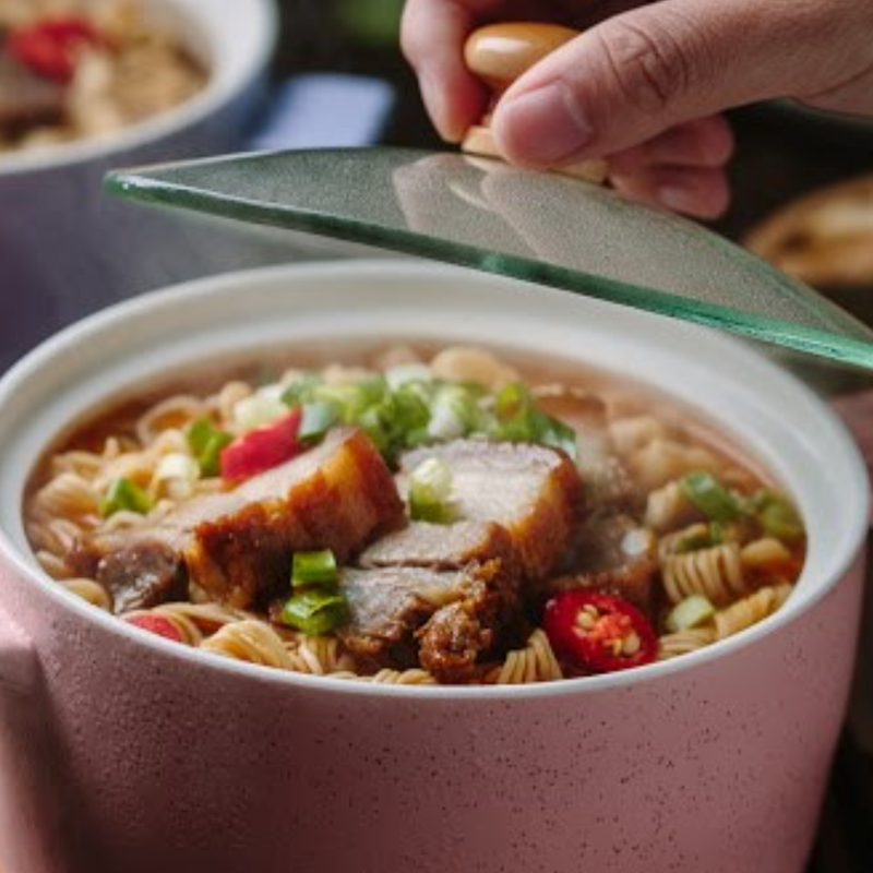 Bowl of noodles with sliced meat and vegetables, being covered with a green lid.