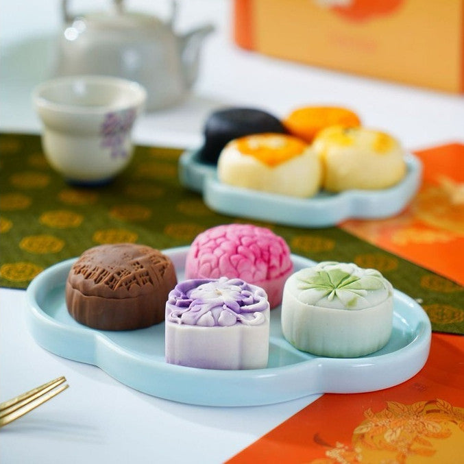 Colorful mooncakes on a tray with a teapot and cups in the background