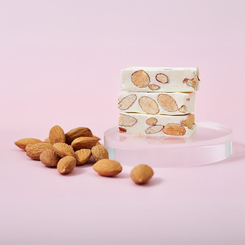 Stack of almond-flavored nougat on a pink background with almonds around