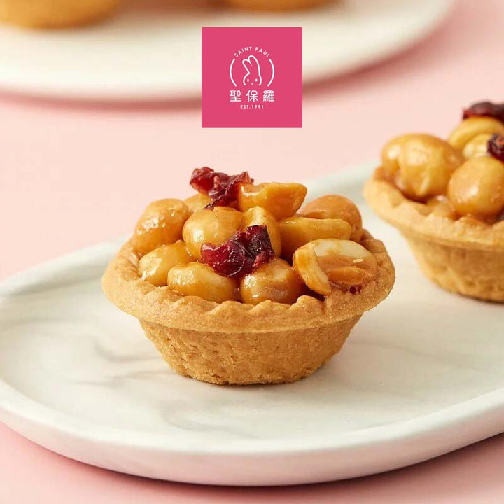Small pastry with nuts and dried fruit on a white plate, with a pink background and brand logo.