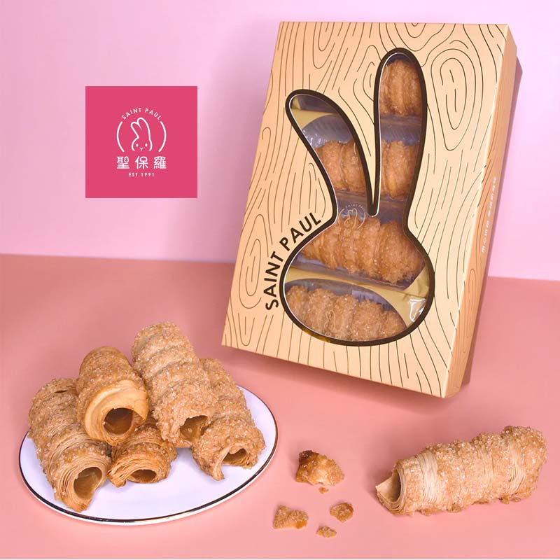 Wooden packaging with 'Saint Paul' branding containing croissant-shaped pastries on a pink background.