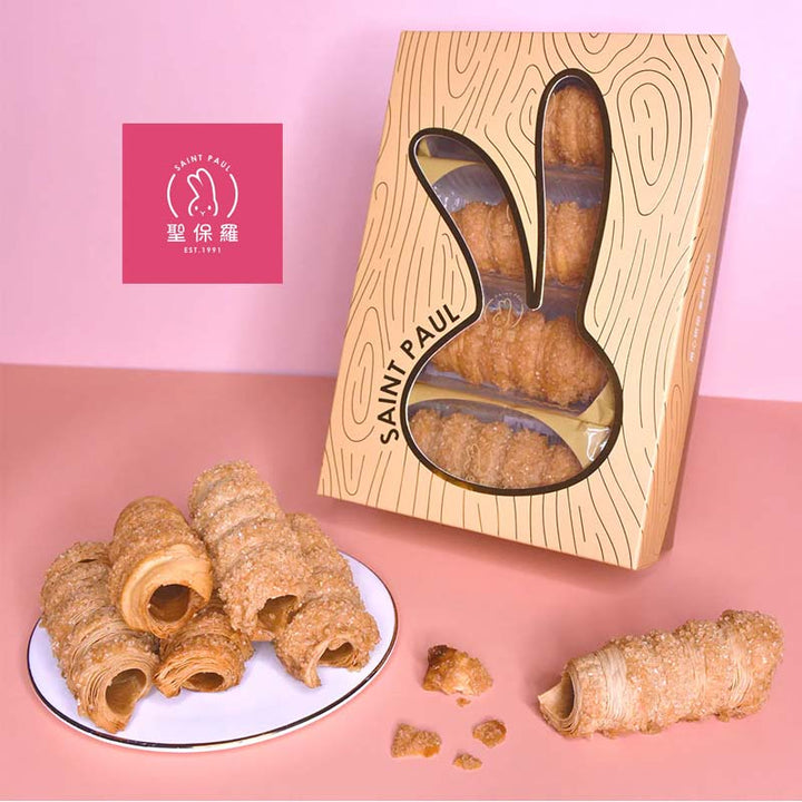 Wooden packaging with 'Saint Paul' branding containing croissant-shaped pastries on a pink background.