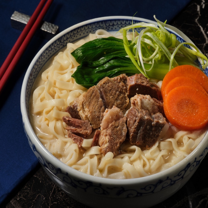 Bowl of ramen with noodles, sliced beef, green onions, and carrots on a dark surface.
